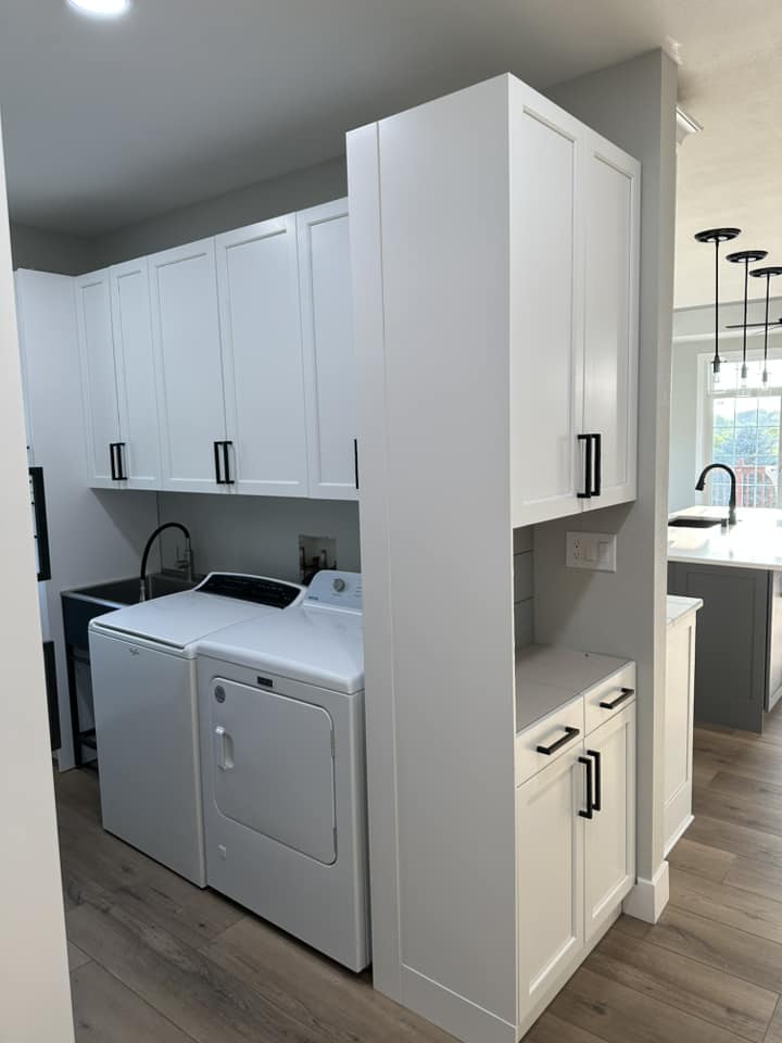 Finished laundry room with white shaker cabinets, black hardware, utility sink, and washer and dryer set